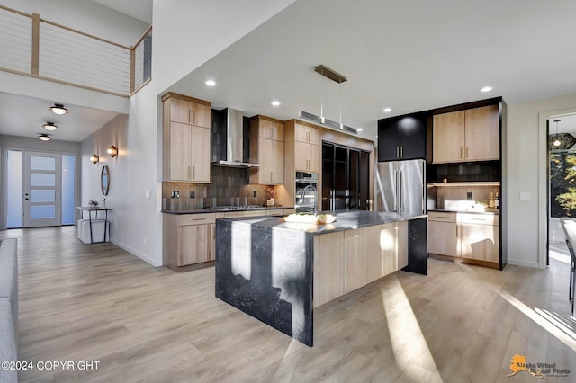 kitchen with hanging light fixtures, a kitchen island with sink, wall chimney exhaust hood, light hardwood / wood-style flooring, and stainless steel appliances