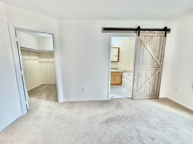 unfurnished bedroom with a closet, a barn door, a spacious closet, light carpet, and ensuite bathroom