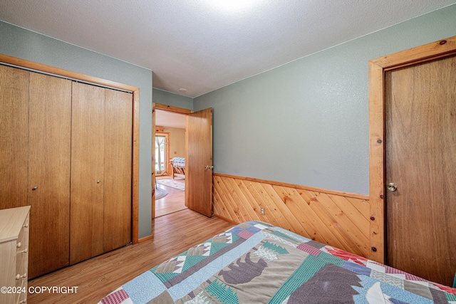 bedroom featuring a closet, light hardwood / wood-style floors, a textured ceiling, and wooden walls