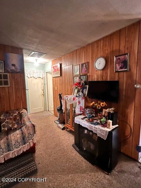 living room with a textured ceiling, wood walls, and carpet flooring