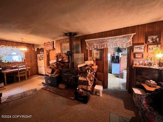 interior space featuring a textured ceiling, a notable chandelier, a wood stove, carpet floors, and wooden walls