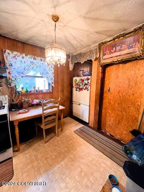 interior space with a textured ceiling, wood walls, stove, and white fridge