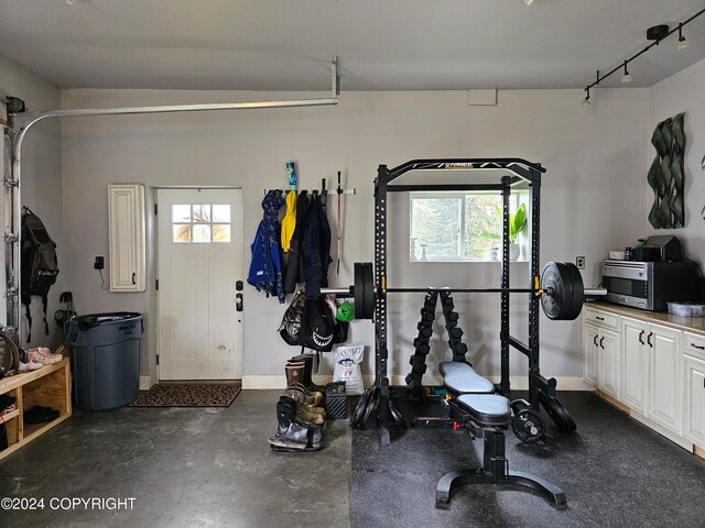 exercise area with a garage, rail lighting, and baseboards