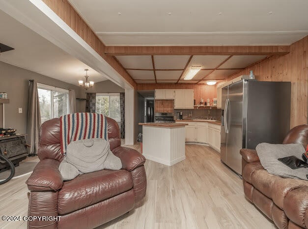 living room featuring beam ceiling, wooden walls, an inviting chandelier, and light hardwood / wood-style flooring