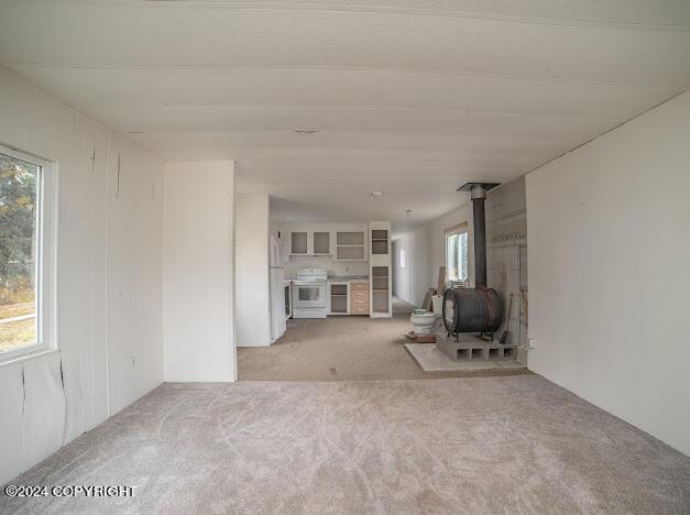 unfurnished living room with light colored carpet, a wood stove, and a wealth of natural light