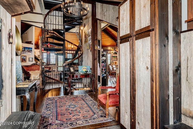 foyer with an inviting chandelier, wood walls, high vaulted ceiling, and hardwood / wood-style flooring