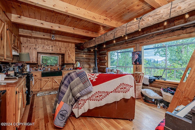 bedroom with multiple windows, light hardwood / wood-style floors, beam ceiling, and a wood stove