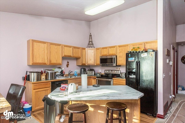 kitchen with sink, black appliances, a center island, a breakfast bar area, and light wood-type flooring