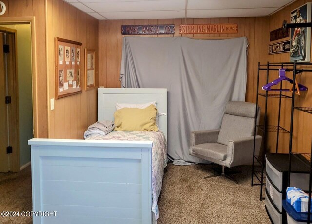 carpeted bedroom featuring a drop ceiling and wooden walls