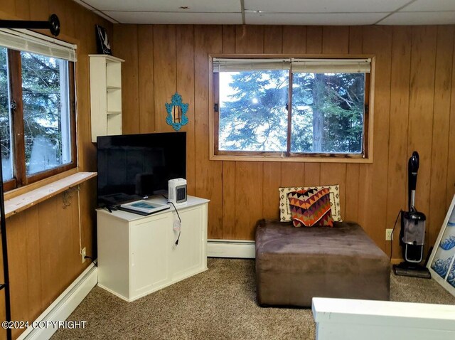 living area featuring carpet, wood walls, a baseboard heating unit, and a paneled ceiling