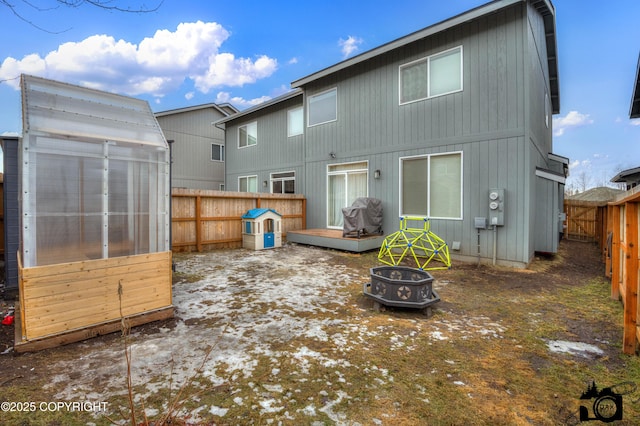 rear view of property with an outdoor fire pit, a greenhouse, a fenced backyard, and an outdoor structure