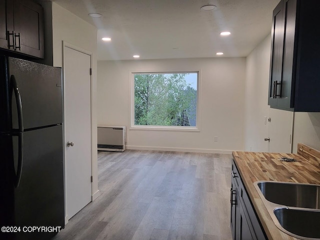 kitchen featuring light hardwood / wood-style floors, wood counters, dark brown cabinets, and black fridge