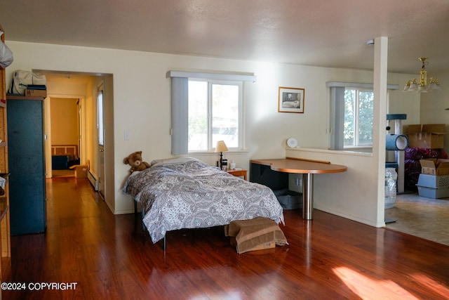 bedroom featuring a notable chandelier, a baseboard heating unit, and dark hardwood / wood-style floors