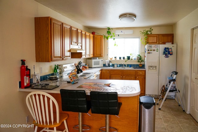 kitchen with light tile patterned floors, sink, kitchen peninsula, white appliances, and a breakfast bar