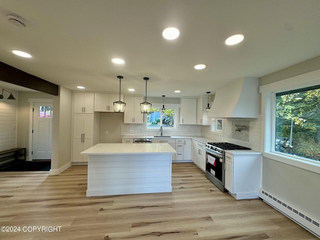 kitchen featuring appliances with stainless steel finishes, custom range hood, white cabinetry, baseboard heating, and pendant lighting