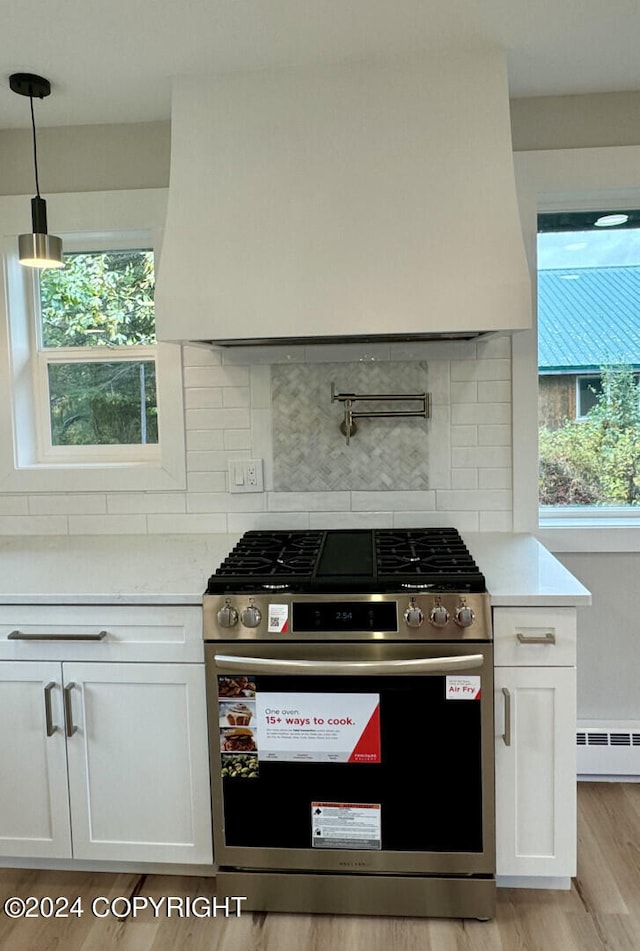 kitchen with white cabinets, high end stainless steel range oven, light hardwood / wood-style floors, and hanging light fixtures