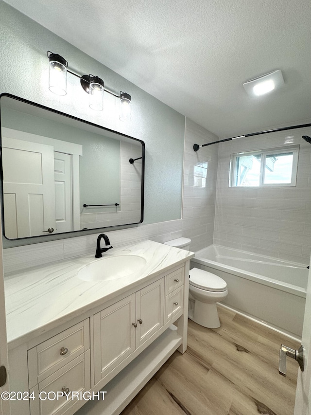 full bathroom featuring vanity, a textured ceiling, tiled shower / bath combo, hardwood / wood-style flooring, and toilet