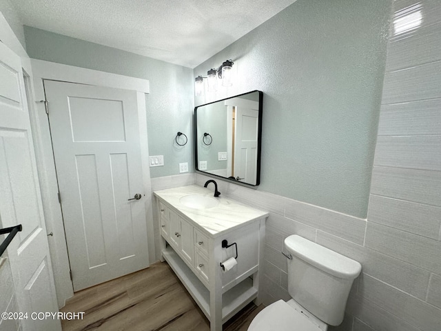 bathroom featuring tile walls, vanity, a textured ceiling, hardwood / wood-style floors, and toilet