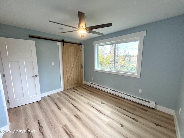 unfurnished bedroom with a barn door, light hardwood / wood-style floors, ceiling fan, and a baseboard radiator