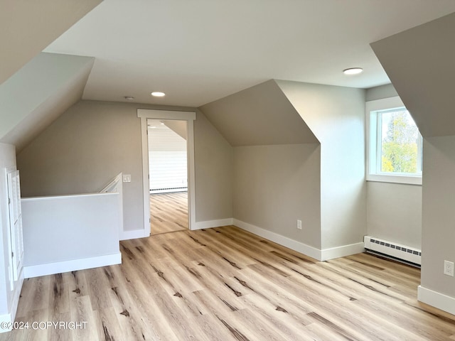 additional living space featuring light wood-type flooring, lofted ceiling, and a baseboard heating unit