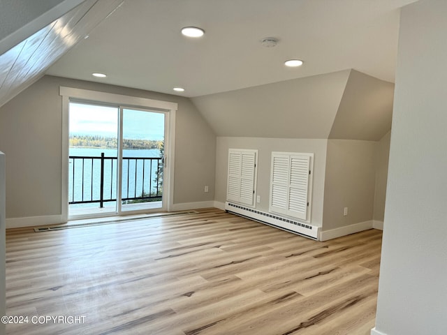 additional living space with a baseboard heating unit, light hardwood / wood-style flooring, a water view, and lofted ceiling