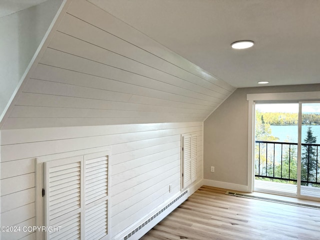 additional living space featuring a water view, vaulted ceiling, a baseboard heating unit, and light hardwood / wood-style flooring