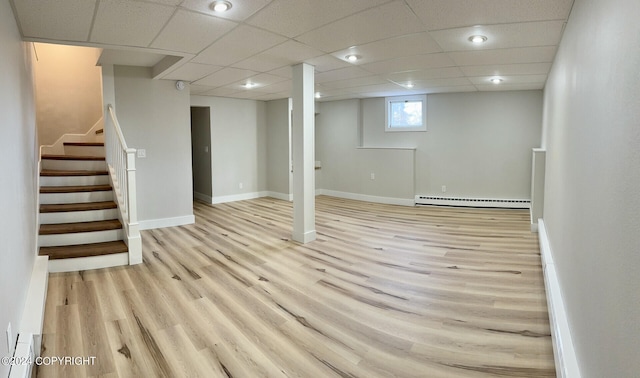 basement featuring light wood-type flooring, a drop ceiling, and a baseboard radiator