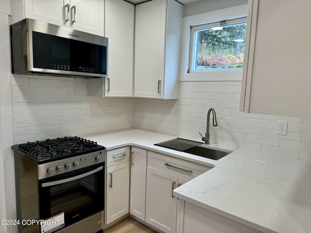 kitchen featuring light stone counters, white cabinets, sink, backsplash, and stainless steel appliances