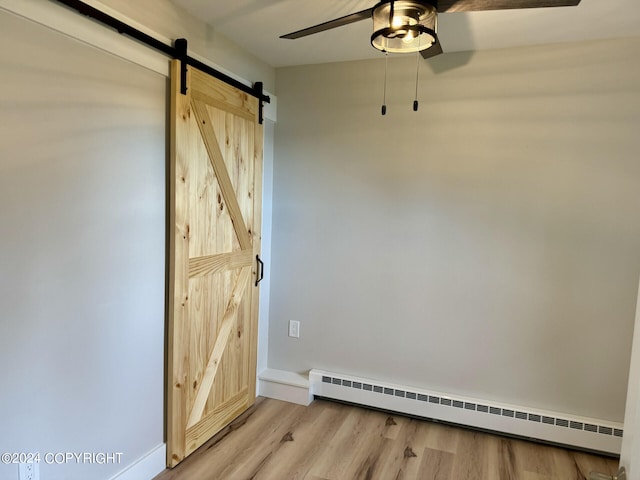 spare room featuring a barn door, ceiling fan, a baseboard heating unit, and hardwood / wood-style flooring