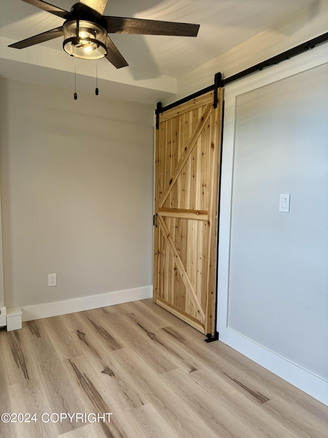 spare room with a barn door, light hardwood / wood-style floors, and ceiling fan