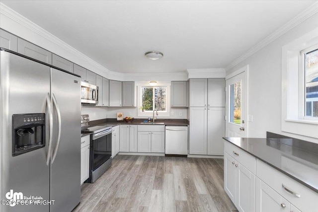 kitchen featuring appliances with stainless steel finishes, light wood-type flooring, ornamental molding, gray cabinets, and sink