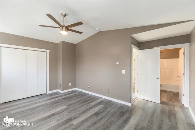 unfurnished bedroom featuring ensuite bath, dark hardwood / wood-style flooring, a closet, ceiling fan, and vaulted ceiling