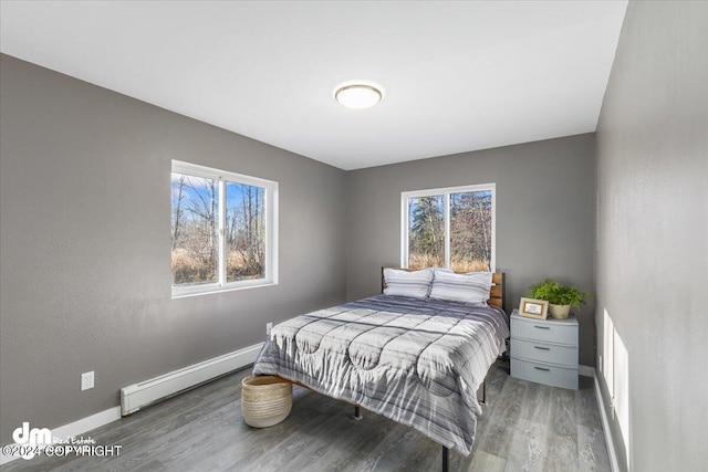 bedroom with multiple windows, baseboard heating, and wood-type flooring