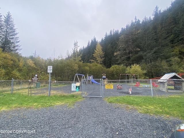view of jungle gym featuring a gate, fence, and a view of trees