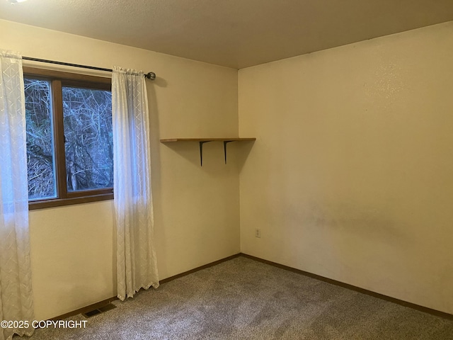 spare room with visible vents, dark colored carpet, and baseboards