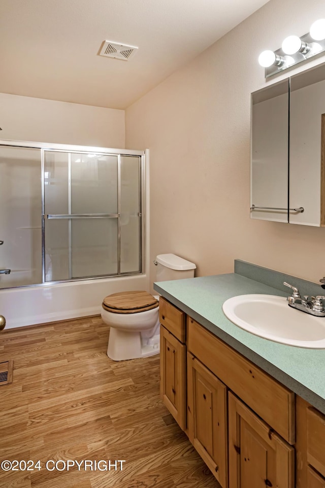 full bathroom with enclosed tub / shower combo, hardwood / wood-style flooring, vanity, and toilet