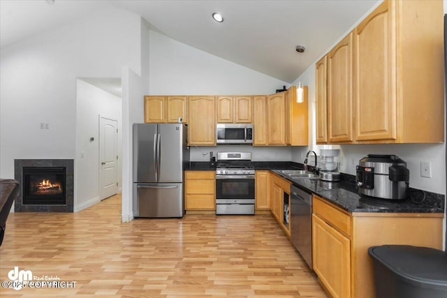 kitchen with sink, dark stone countertops, stainless steel appliances, light hardwood / wood-style floors, and light brown cabinetry