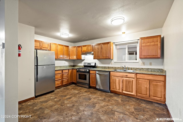 kitchen featuring brown cabinetry, baseboards, a sink, under cabinet range hood, and appliances with stainless steel finishes