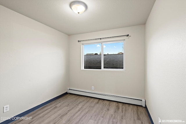 empty room featuring wood finished floors, baseboards, and baseboard heating