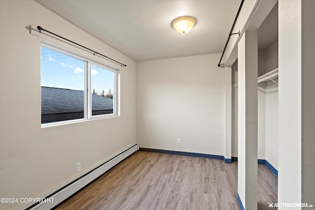 unfurnished bedroom featuring a baseboard heating unit, light wood-style floors, and baseboards