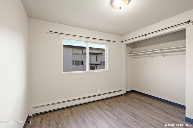 unfurnished bedroom featuring a closet, baseboard heating, and wood finished floors