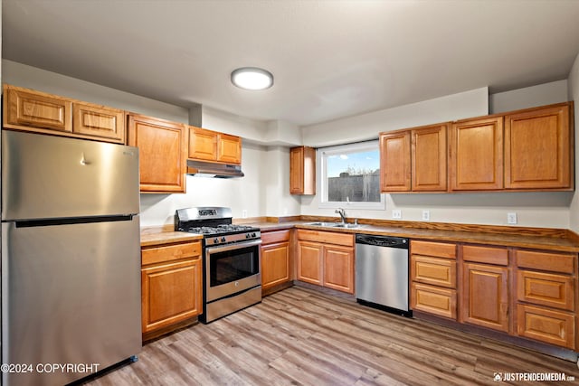 kitchen with under cabinet range hood, light wood-style flooring, brown cabinets, stainless steel appliances, and a sink