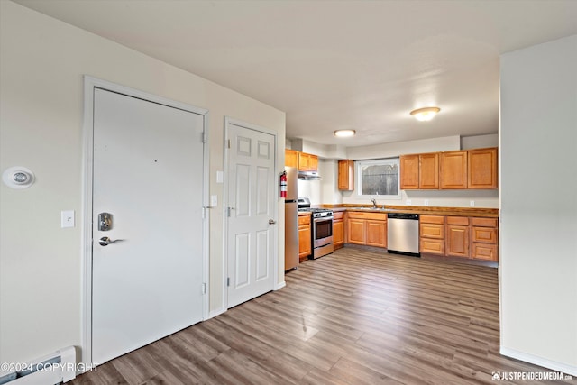 kitchen featuring under cabinet range hood, a sink, wood finished floors, stainless steel appliances, and baseboard heating