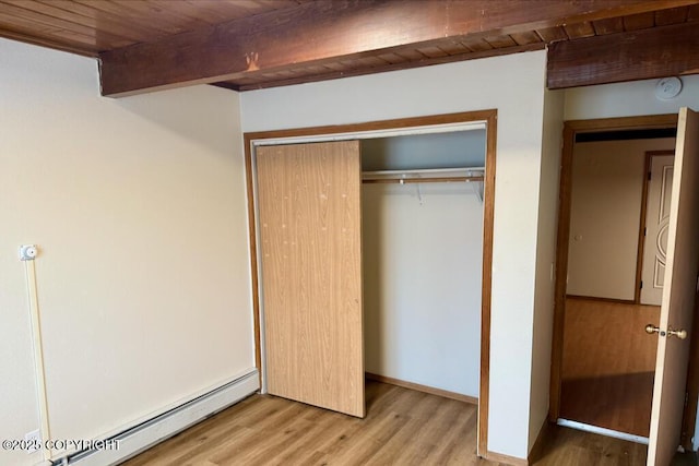 unfurnished bedroom featuring beam ceiling, wooden ceiling, wood finished floors, a closet, and a baseboard radiator