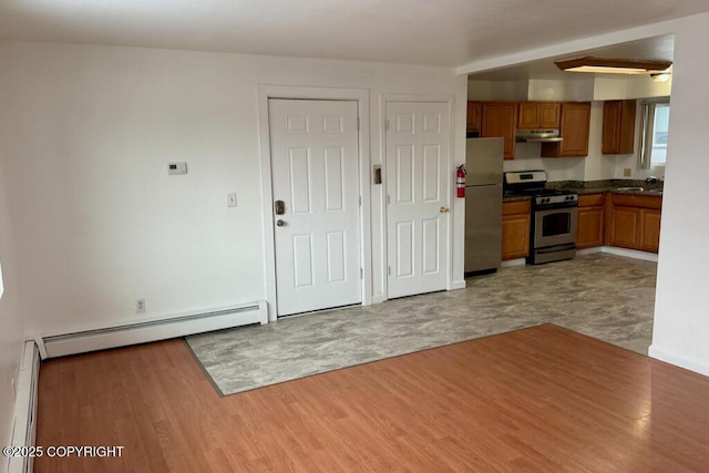 kitchen with a baseboard radiator, under cabinet range hood, appliances with stainless steel finishes, brown cabinets, and baseboard heating