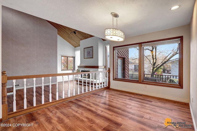 empty room with lofted ceiling, hardwood / wood-style floors, a textured ceiling, and a healthy amount of sunlight