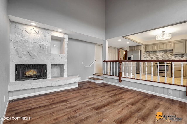 unfurnished living room featuring a stone fireplace, hardwood / wood-style flooring, and a towering ceiling