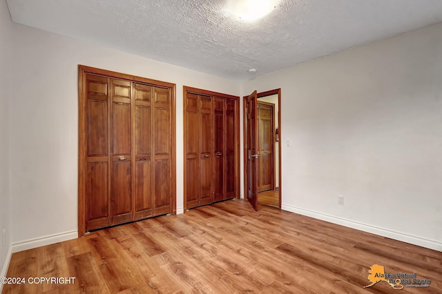 unfurnished bedroom featuring a textured ceiling, two closets, and light wood-type flooring