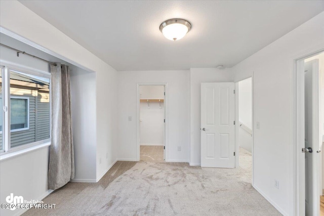 unfurnished bedroom featuring a closet, light colored carpet, and a walk in closet