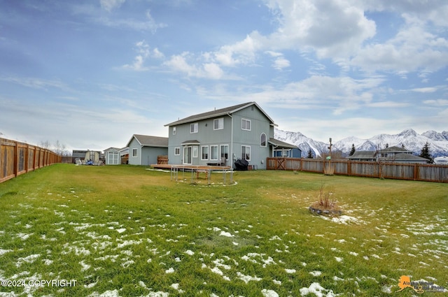 rear view of house with a mountain view, a trampoline, and a yard